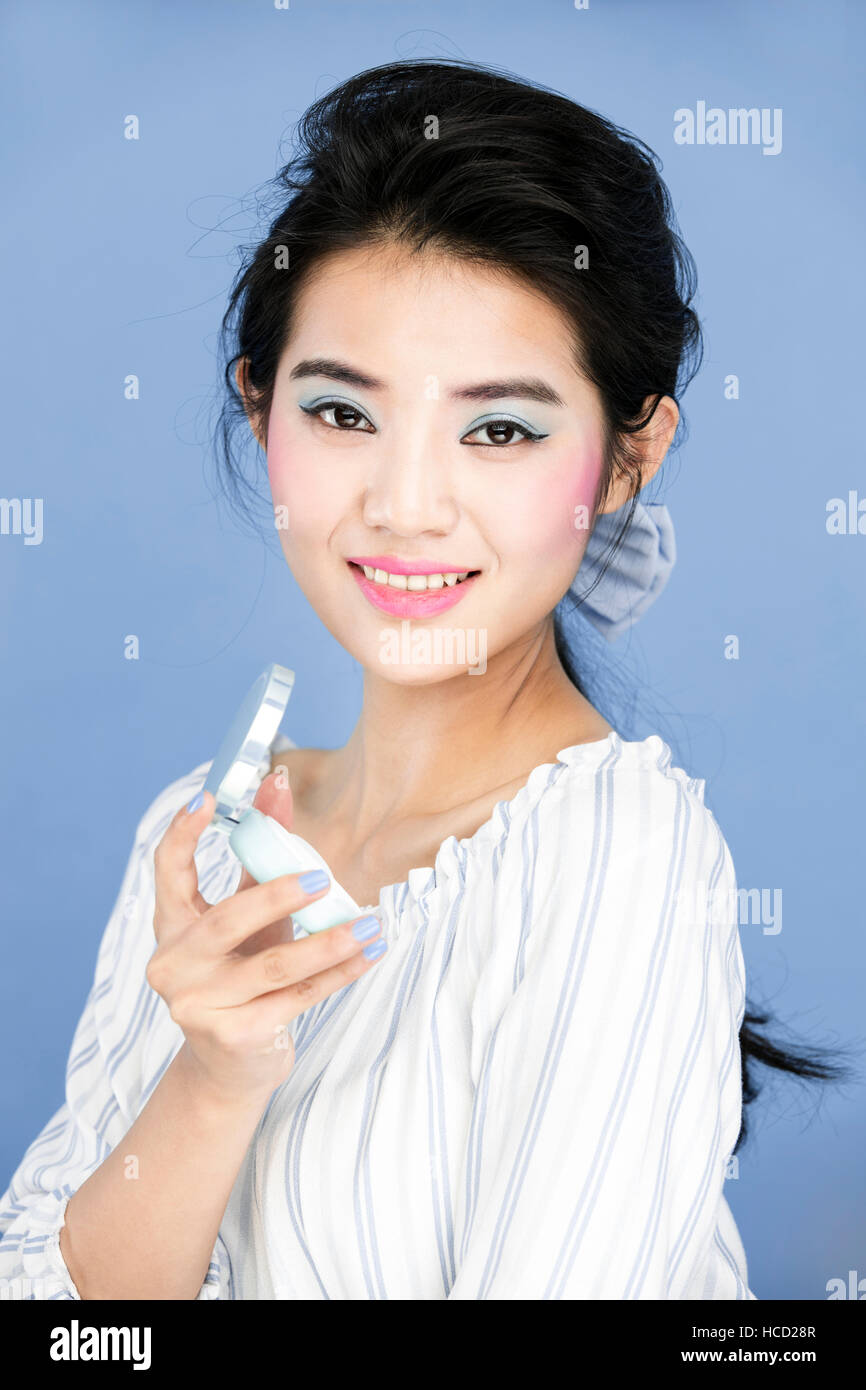 Ritratto di giovane donna con polvere compatta contro la serenità Foto Stock
