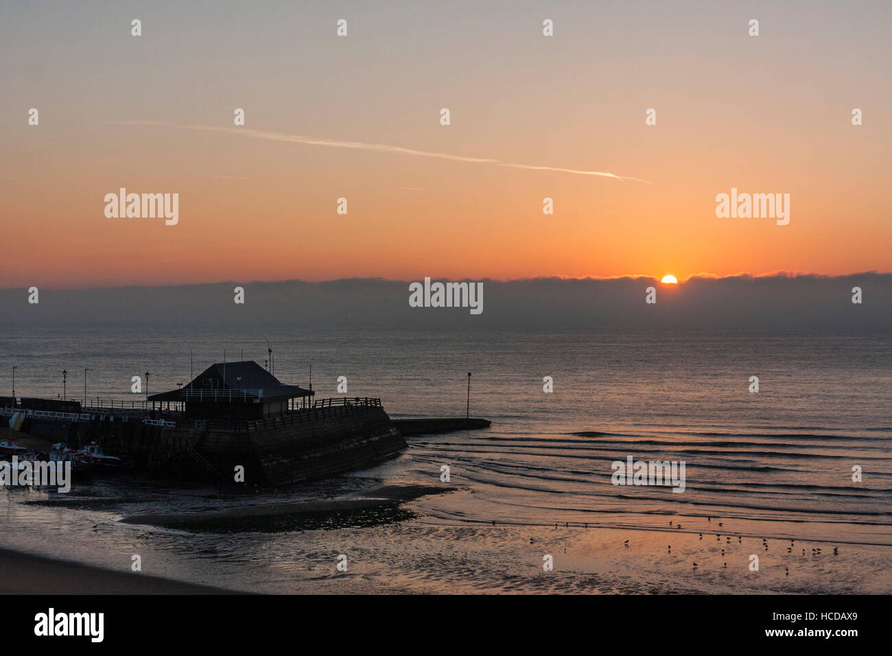 Inghilterra, Broadstairs. Dawn, sunrise la rottura oltre il Canale della Manica e il porto di silhouette. Foto Stock