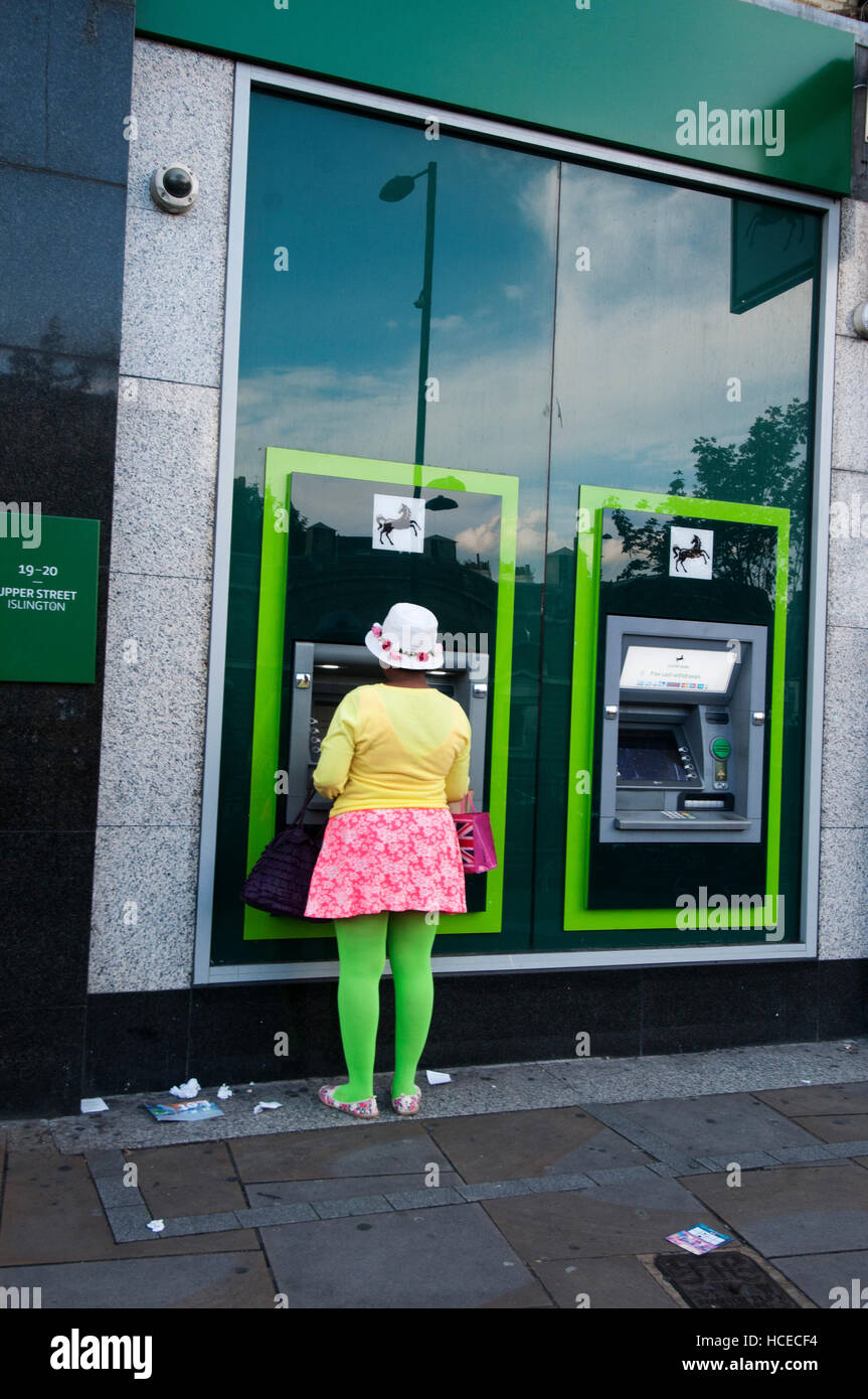 Islington. Un colorfully vestito donna presso un Bancomat presso la Lloyds Bank. Foto Stock