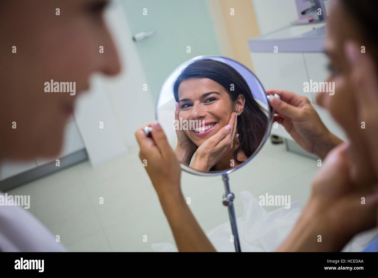 Donna controllando la sua pelle nello specchio dopo aver ricevuto un trattamento cosmetico Foto Stock