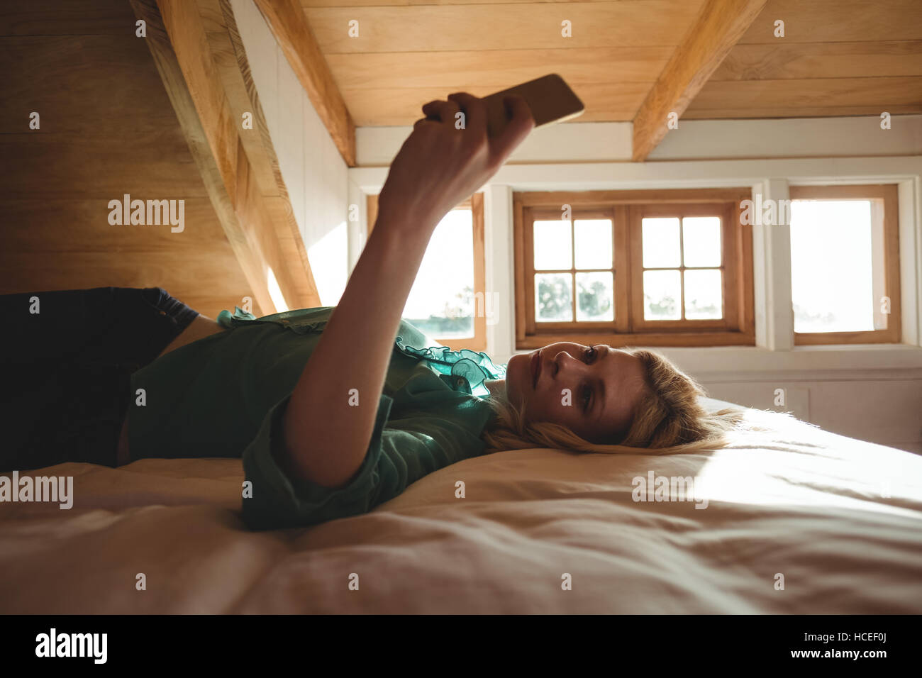 Bella donna sdraiata sul letto e utilizzando il telefono cellulare in camera da letto Foto Stock