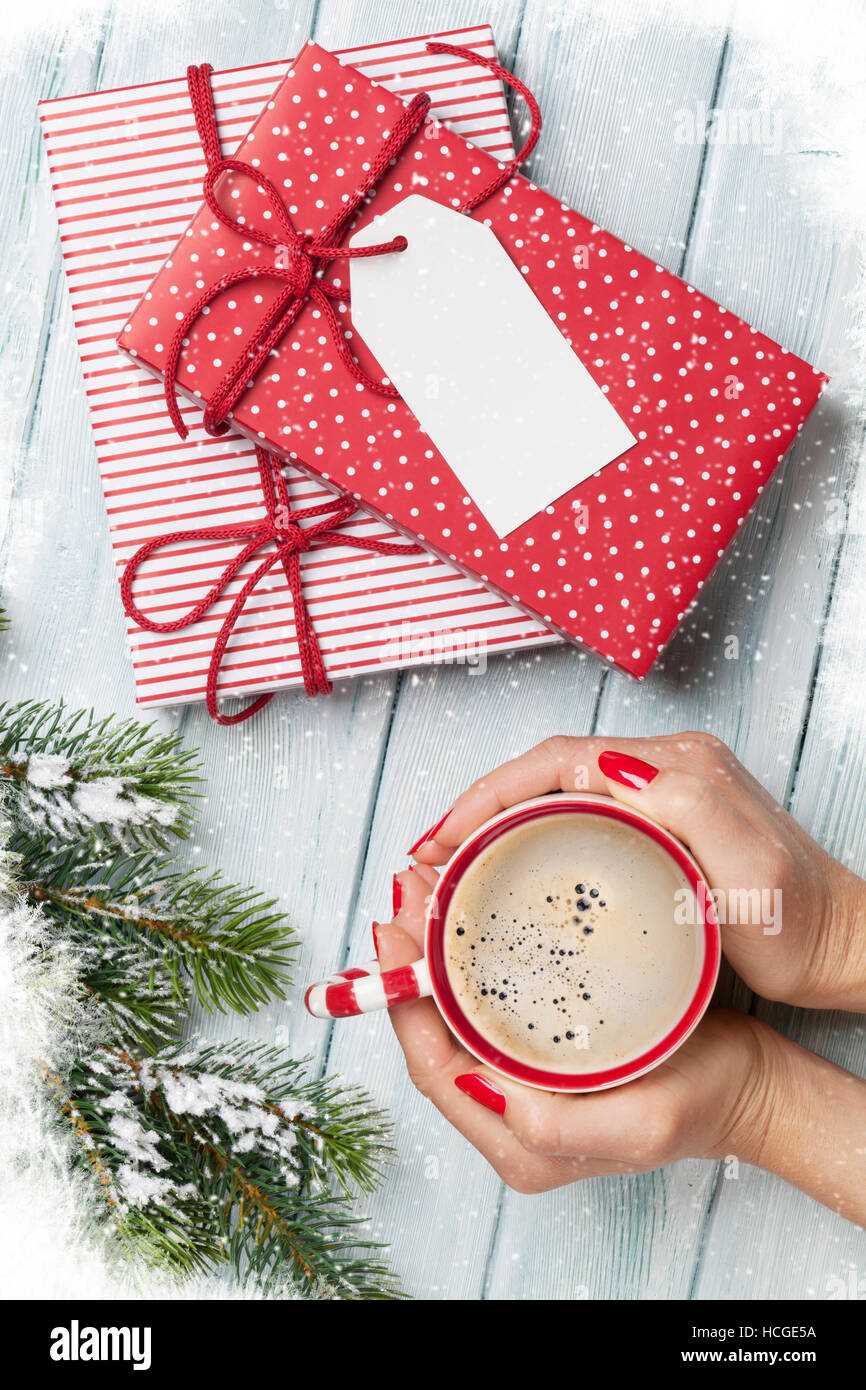 Mani femminili holding tazza da caffè, natale confezioni regalo e neve abete al di sopra di un tavolo di legno. Vista da sopra con lo spazio di copia Foto Stock