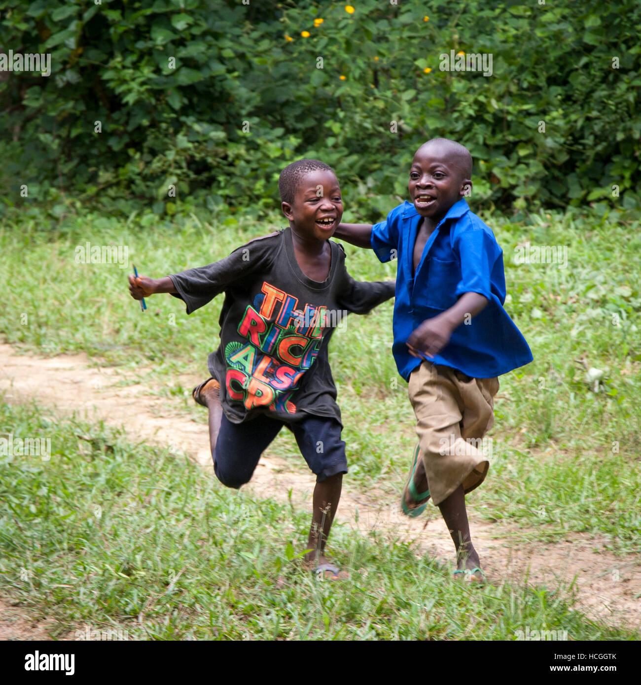 Due ragazzi della Sierra Leone sono felici, che corrono attraverso il loro villaggio rurale. La t-shirt indica: 'Anche i ricchi piangono'. Due poveri ragazzi che corrono e godono della vita. Nella zona di Gola vivono persone della tribù Mendy. Un ragazzo indossa la divisa della scuola, l'altro ha penne in mano e indossa una maglietta, che probabilmente gli è stata data dai viaggiatori. Foto Stock