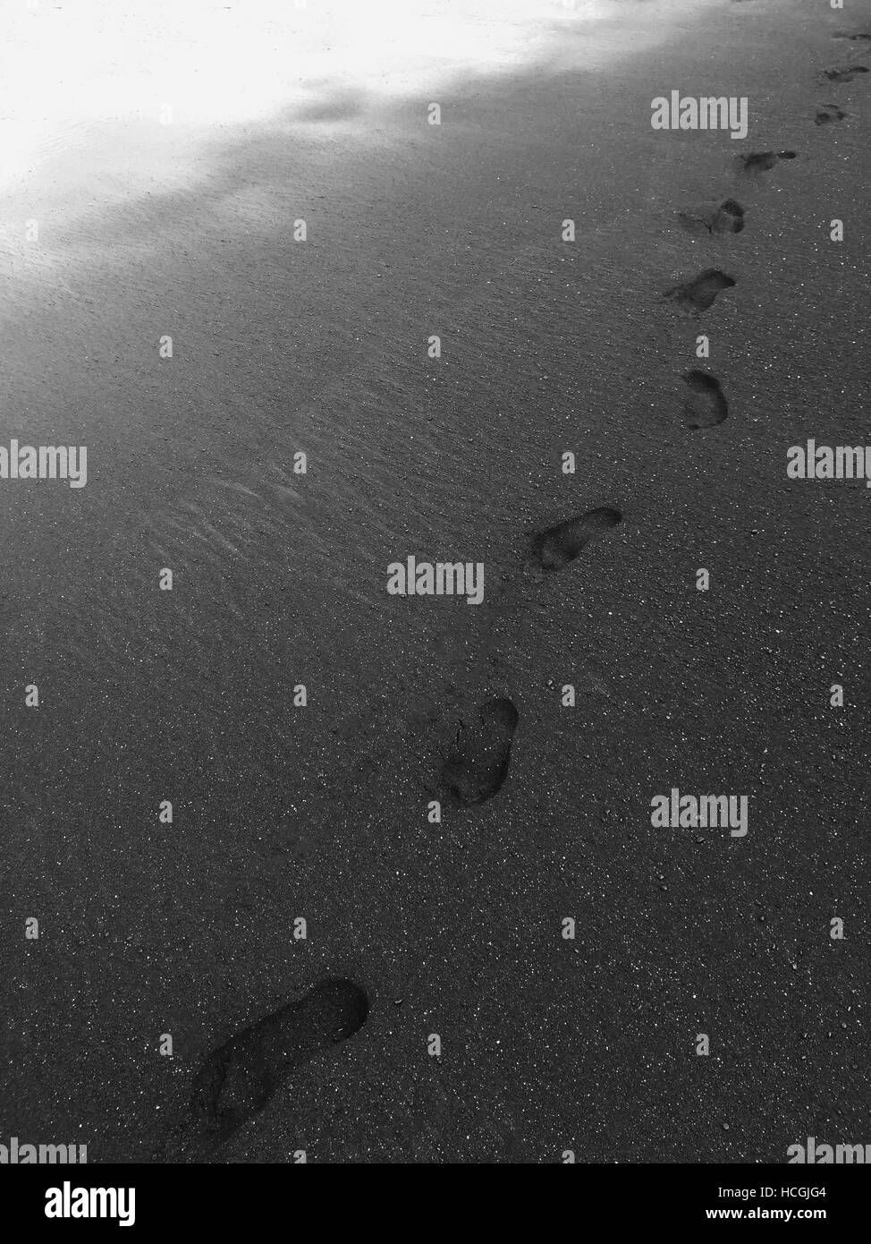 Footprints dopo lone camminare sulla spiaggia di sabbia nera dall'oceano - Maui, Hawaii Foto Stock