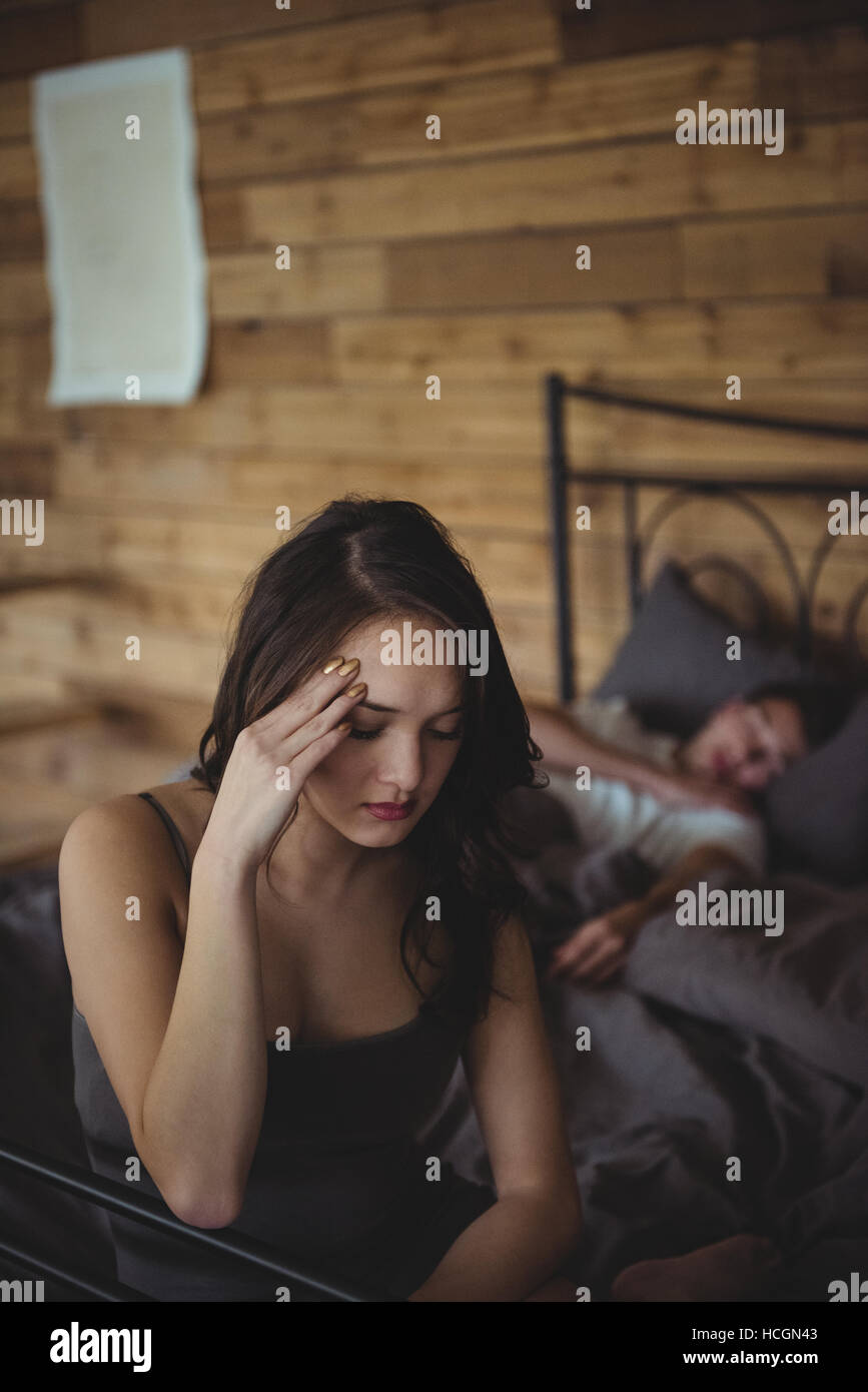 Sconvolto donna seduta su un letto mentre l uomo dorme in background Foto Stock