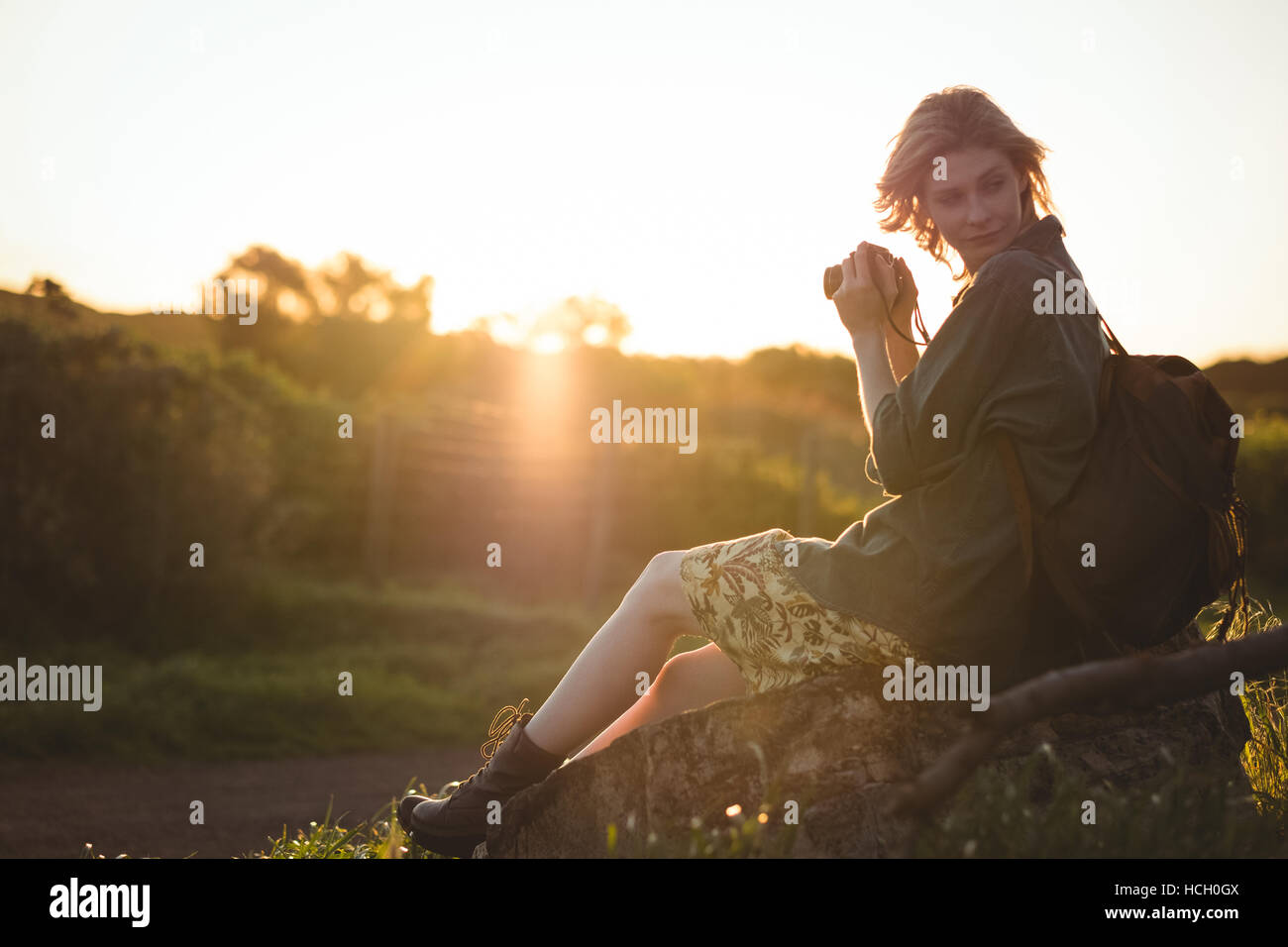 Premurosa donna seduta su roccia e tenendo la fotocamera digitale Foto Stock