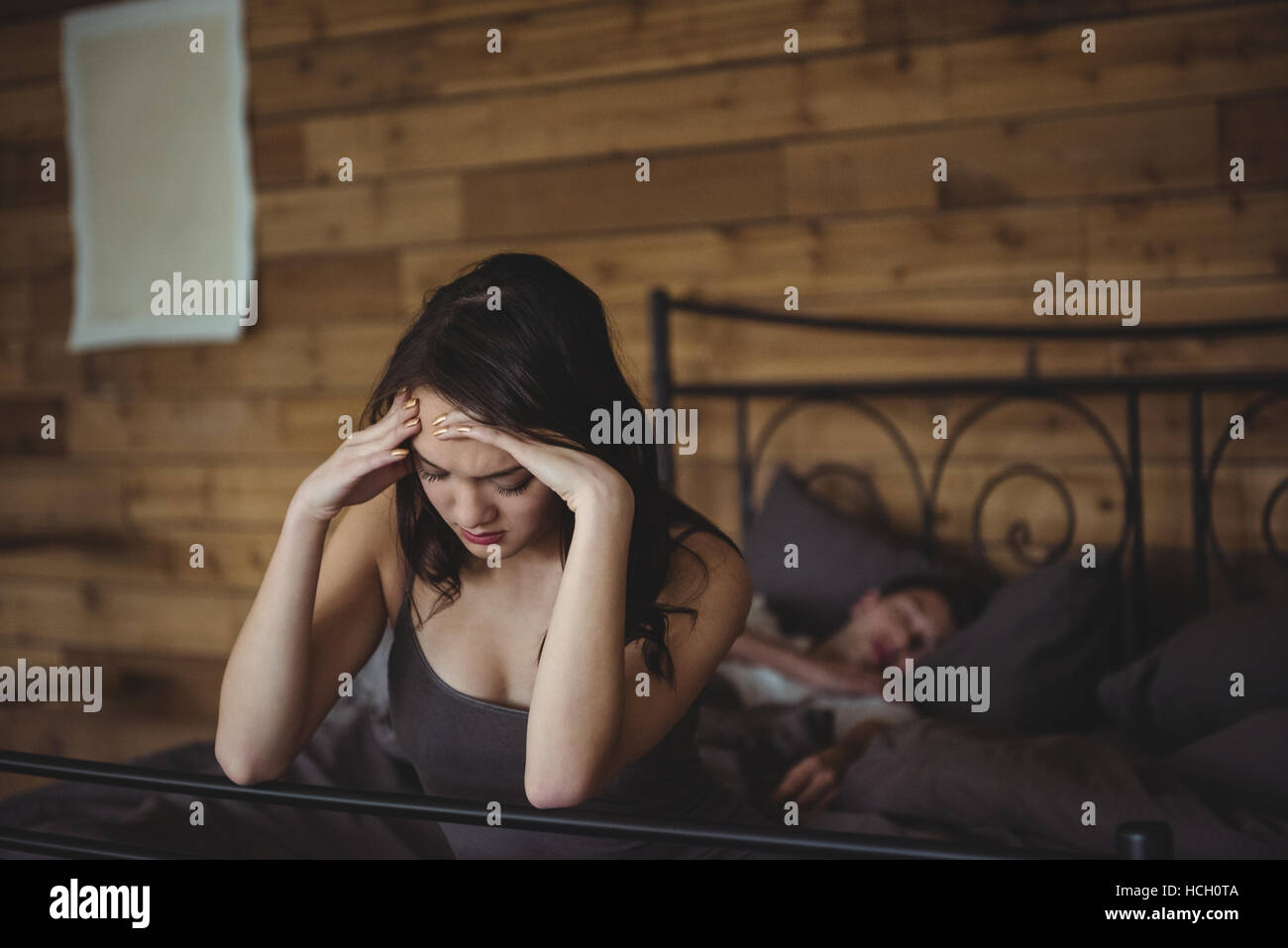Sconvolto donna seduta su un letto mentre l uomo dorme in background Foto Stock