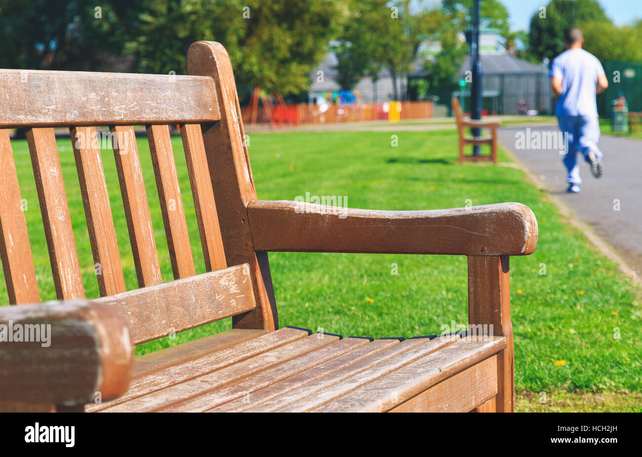 Pubblica banco di legno con un pareggiatore in background in un parco Foto Stock