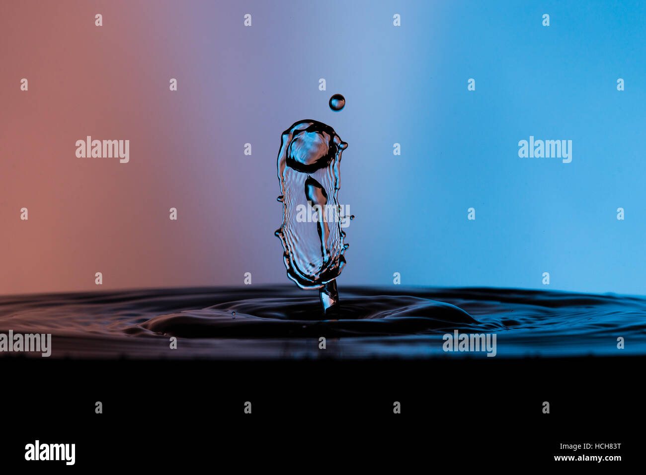 Goccia di acqua splash con una lunga area di goccioline che guarda come i capelli con arancia e sfondo blu Foto Stock