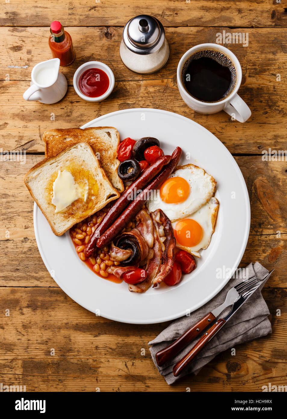 La completa prima colazione Inglese con uova fritte, salsicce, pancetta, fagioli, pane tostato, pomodori e funghi su sfondo di legno Foto Stock