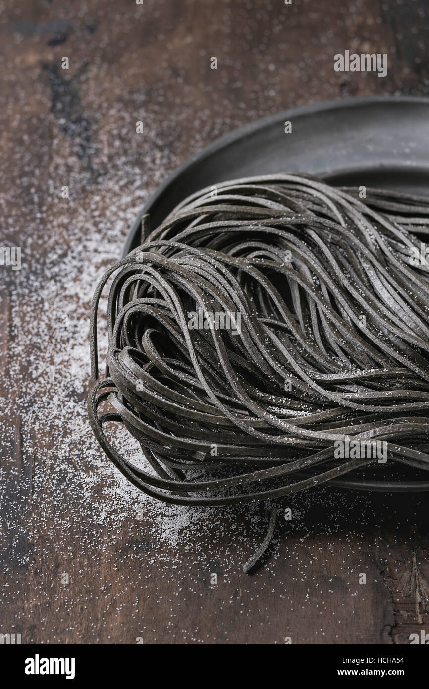 Materie non cotti nero inchiostro seppia spaghetti con farina su vintage piastra metallica sul legno scuro dello sfondo. Con spazio per il testo. Foto Stock