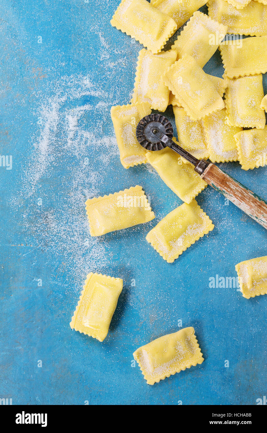 Fatta fresca materie non cotti italiano ravioli di pasta con farina e vintage taglia pasta su blu luminoso sullo sfondo di legno. Vista da sopra con copia spazio. Foto Stock