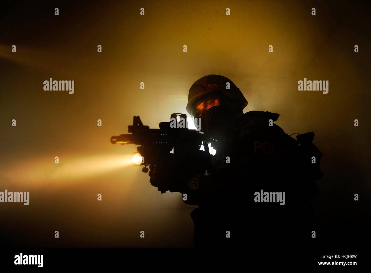 Una speciale selezione di armi e tattiche (SWAT) squadra dimostra come cancellare le camere utilizzando fumo e torce elettriche di manovra. Un funzionario di polizia si guarda intorno la camera per possibili sospetti utilizzando la torcia sul suo semi-arma automatica. Foto Stock
