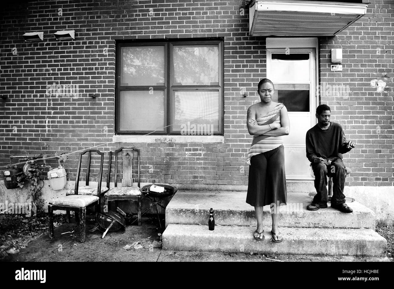 Una donna e suo fratello sedersi sulla loro veranda in sede di governo. Vecchio e sedie rotte, bottiglie di birra e cestino piccolo cortile anteriore. Foto Stock