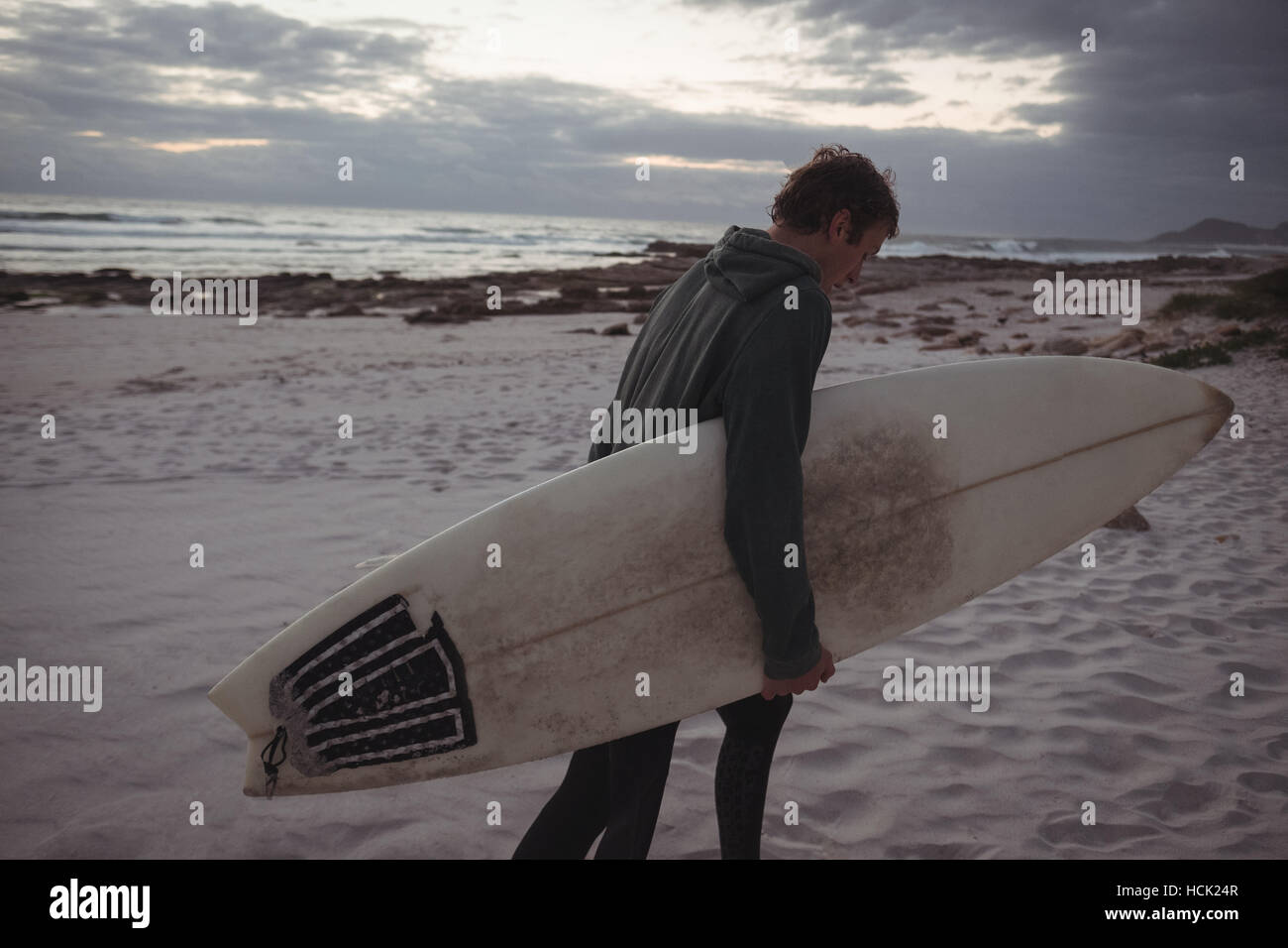 Uomo che porta la tavola da surf a piedi sulla spiaggia Foto Stock