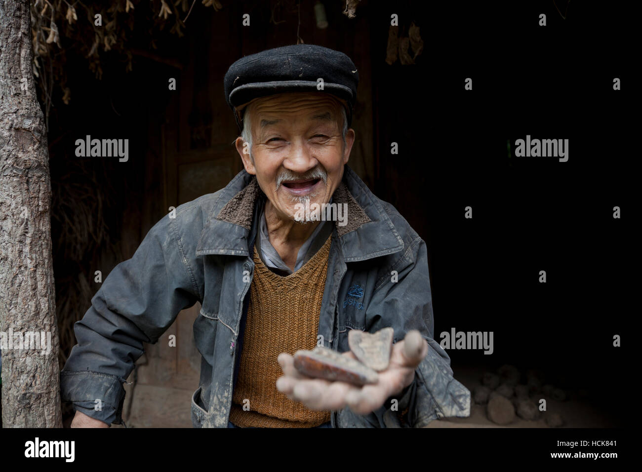 Un vecchio contadino in un piccolo villaggio nella Cina occidentale esce tenendo un paio di essa-grammi di legno nella sua mano tesa. Foto Stock