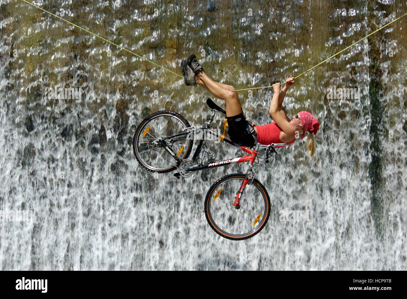 Donna attraversando una cascata su una corda con una bici Foto Stock