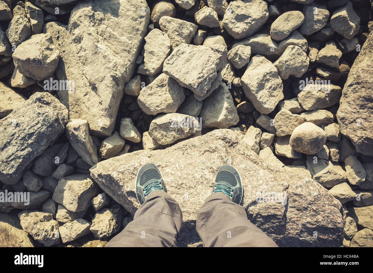 Piedini maschio in tela blu scarpe sportive permanente sulla costiera rocciosa irregolare di massa. Travel lifstyle sfondo. Annata calda tonalità foto filtro, o Foto Stock