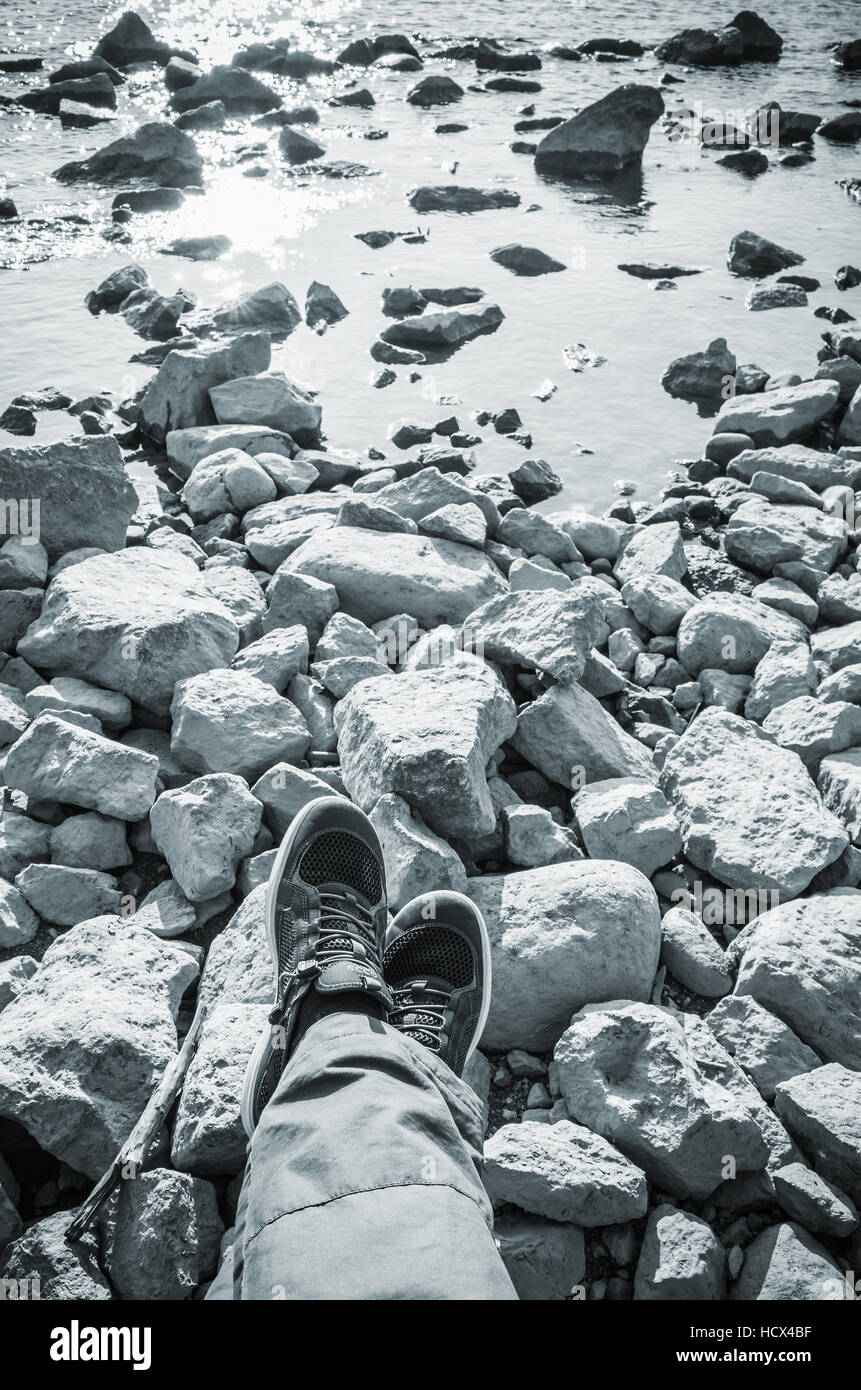 Piedini maschio in tela blu scarpe sportive permanente sulla costiera rocciosa irregolare di massa. Corsa verticale lifstyle sfondo. Nei toni del blu, filtro foto Foto Stock