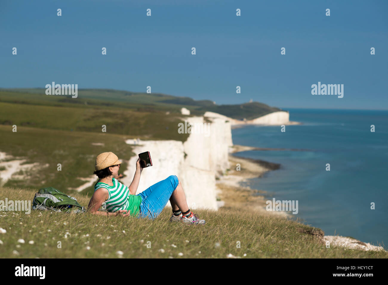 Una donna che legge il suo iPad sulla scogliera con viste delle Sette sorelle del litorale, South Downs National Park, East Sussex, Regno Unito Foto Stock