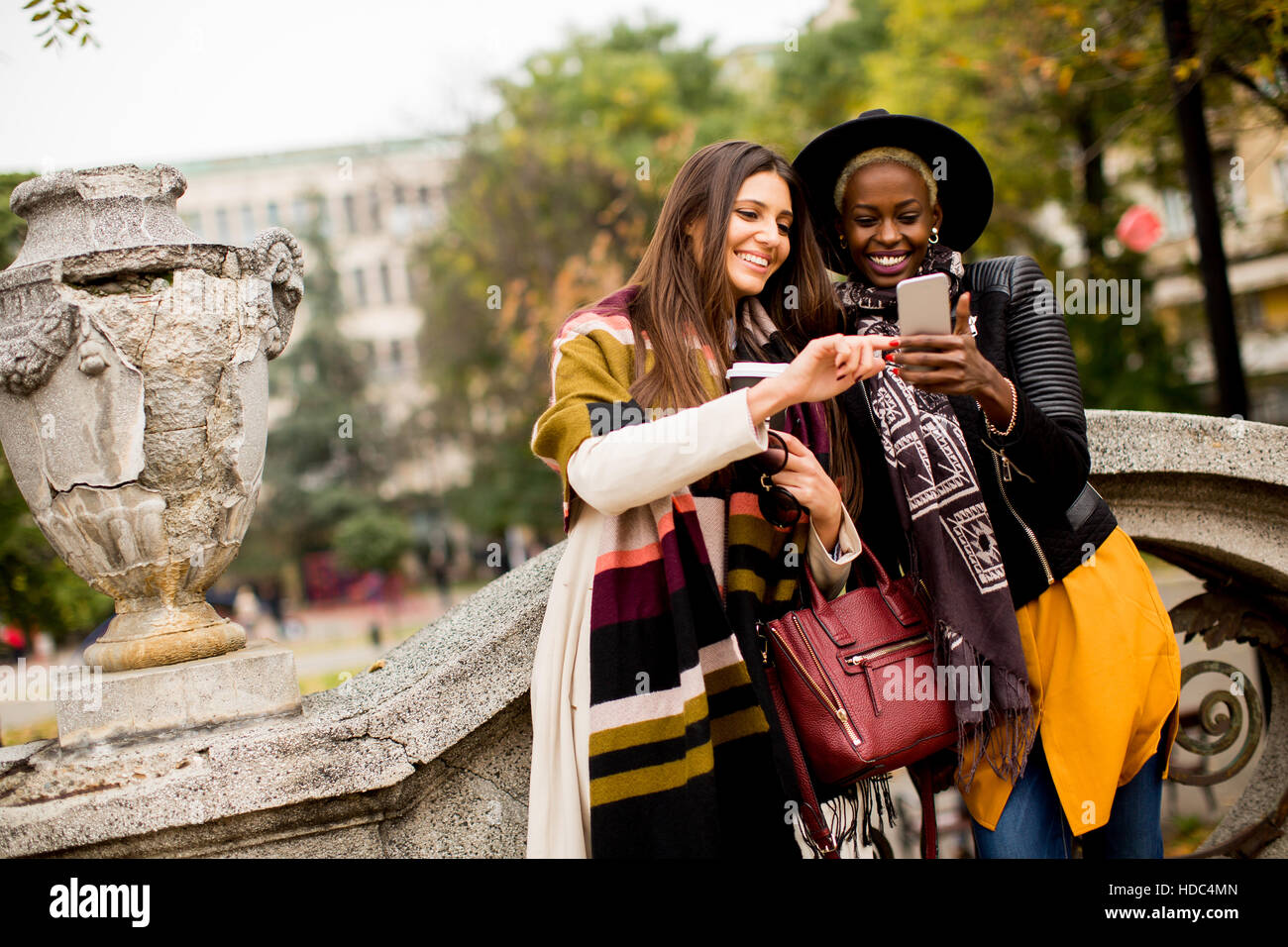 Americano africano e caucasici che pongono la donna fuori con il telefono cellulare e una tazza di caffè per andare in autunno Foto Stock