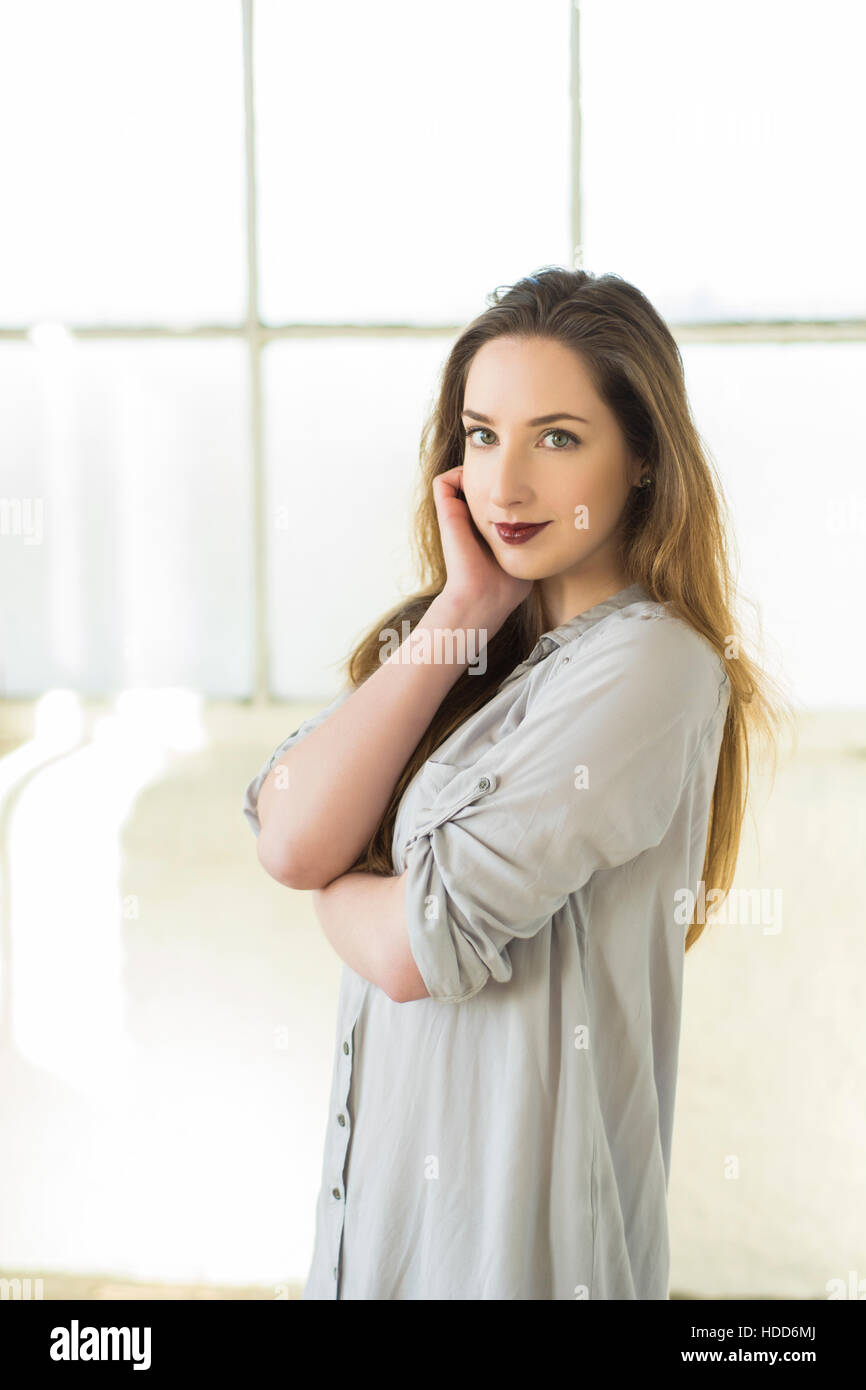 Bella giovane donna con capelli scuri in piedi vicino alla finestra Mano faccia toccante Foto Stock