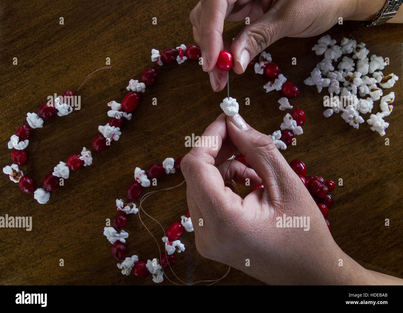 Close up donna ponendo le mani di popcorn e un mirtillo rosso fresco su un ago e filo da aggiungere a ghirlanda di Natale. Foto Stock