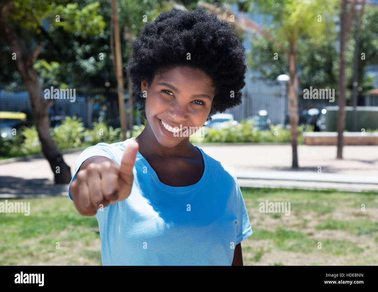 Felice African American Girl mostra il pollice all'aperto in un parco in estate Foto Stock