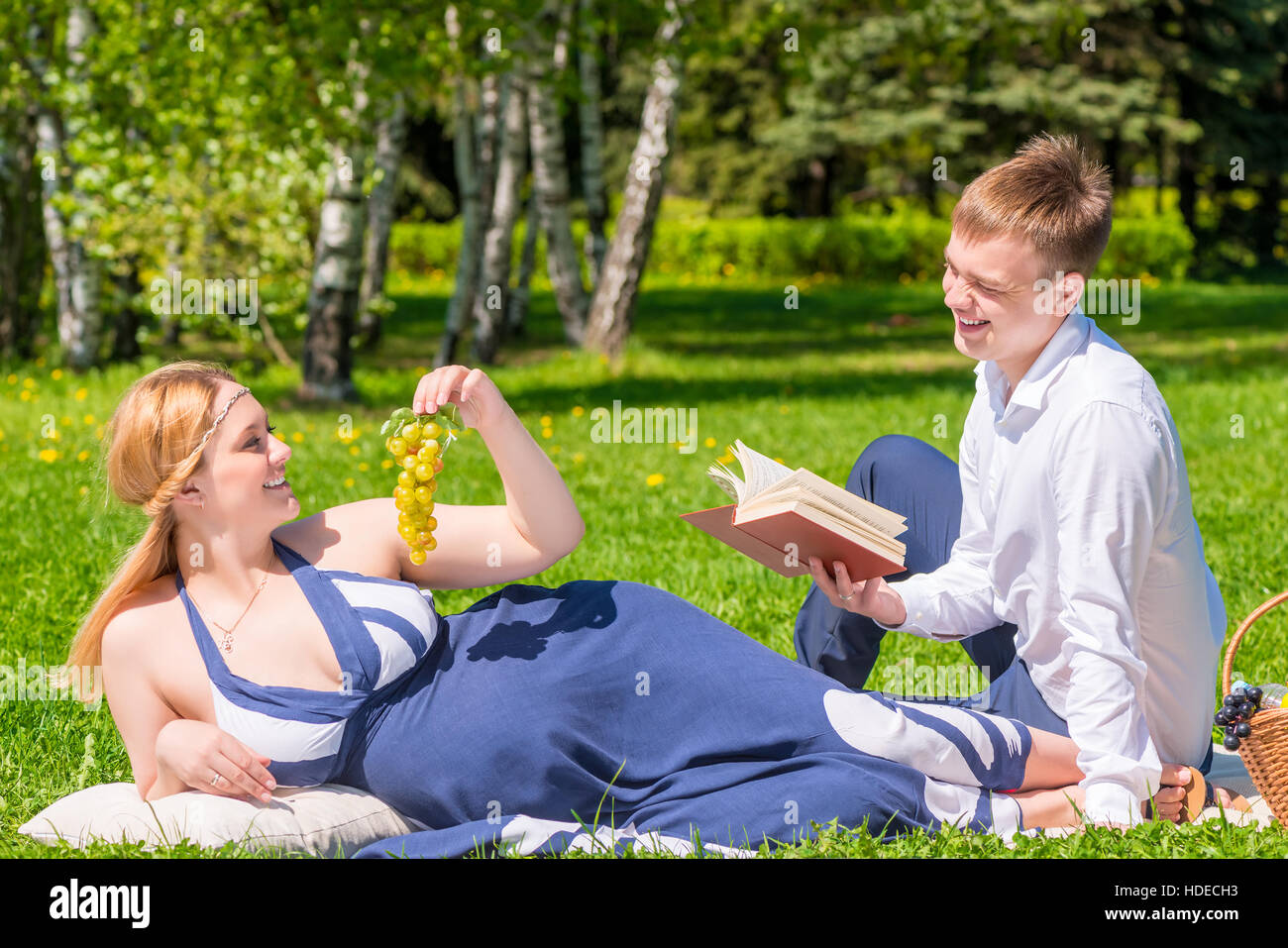 Donna incinta con uva e il marito con un libro del picnic Foto Stock