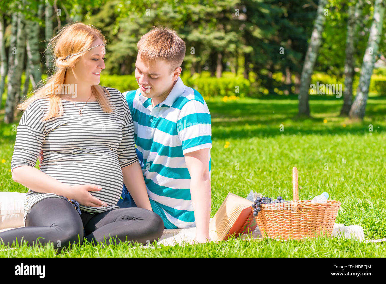 Famiglia giovane di riposo in un parco a un picnic, la ragazza con una grande pancia in gravidanza Foto Stock