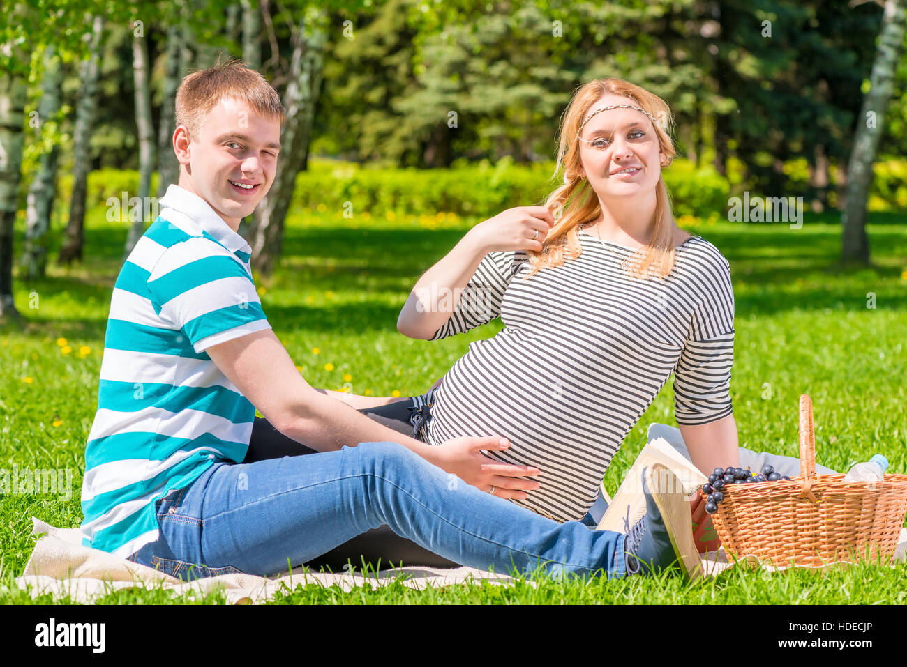 Giovane e bella famiglia avente un picnic nel parco, la donna è in stato di gravidanza Foto Stock