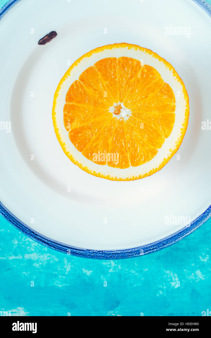 La metà di colore arancione sulla piastra bianca sul ciano verticale di sfondo Foto Stock