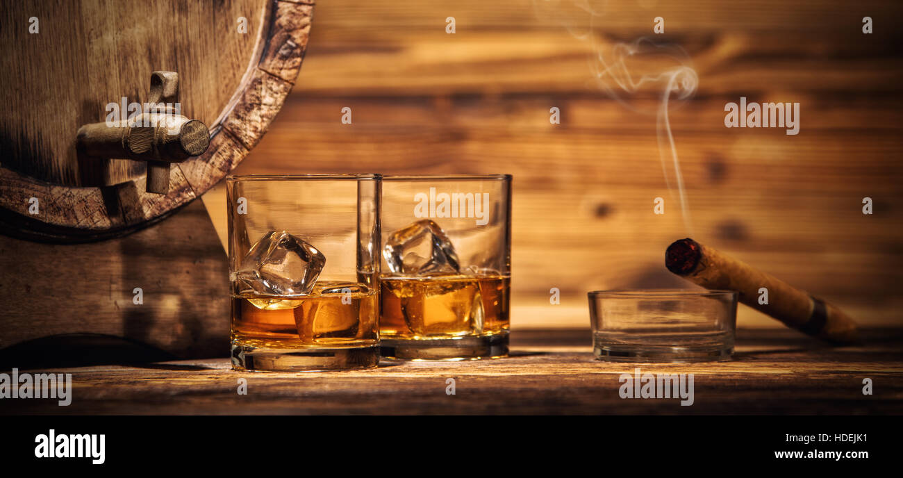 Due bicchieri di whiskey con cubetti di ghiaccio servita su tavole di legno con il barile. Vintage il ripiano del bancone con evidenziazione e bicchieri di liquore duro Foto Stock