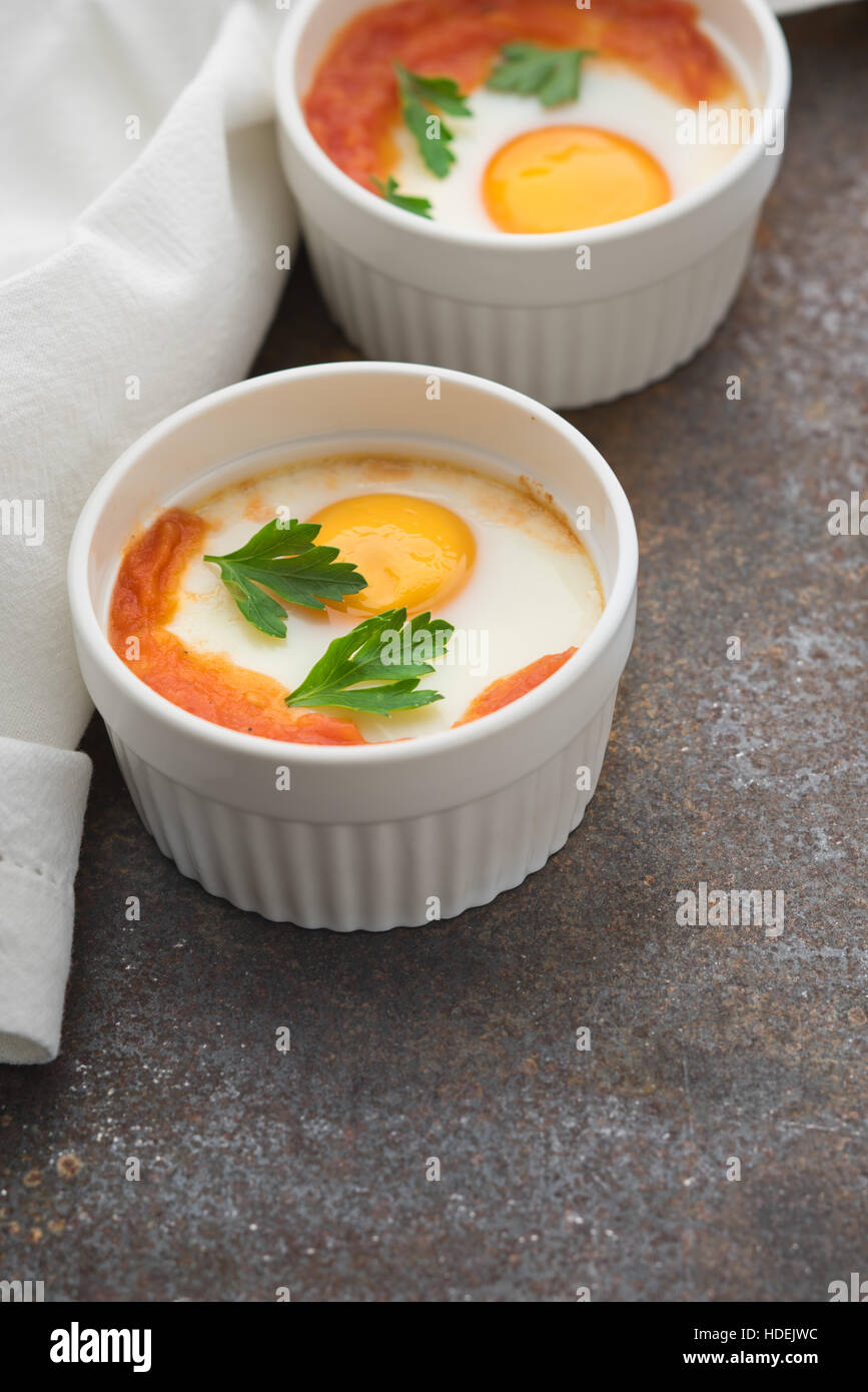 Uova al forno con pomodori e prezzemolo in verticale ramekins Foto Stock