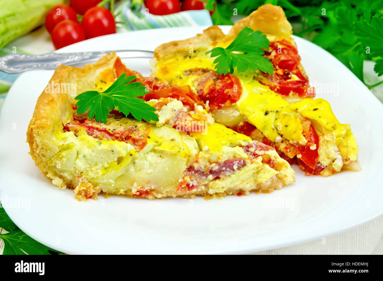 Due pezzi di torta di zucchine con i pomodori e le uova in una piastra bianca su un tovagliolo, prezzemolo su tavole di legno sfondo Foto Stock