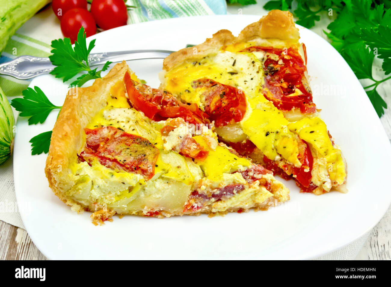 Due pezzi di torta di zucchine con i pomodori e le uova in un piatto su un tovagliolo, prezzemolo su tavole di legno sfondo Foto Stock