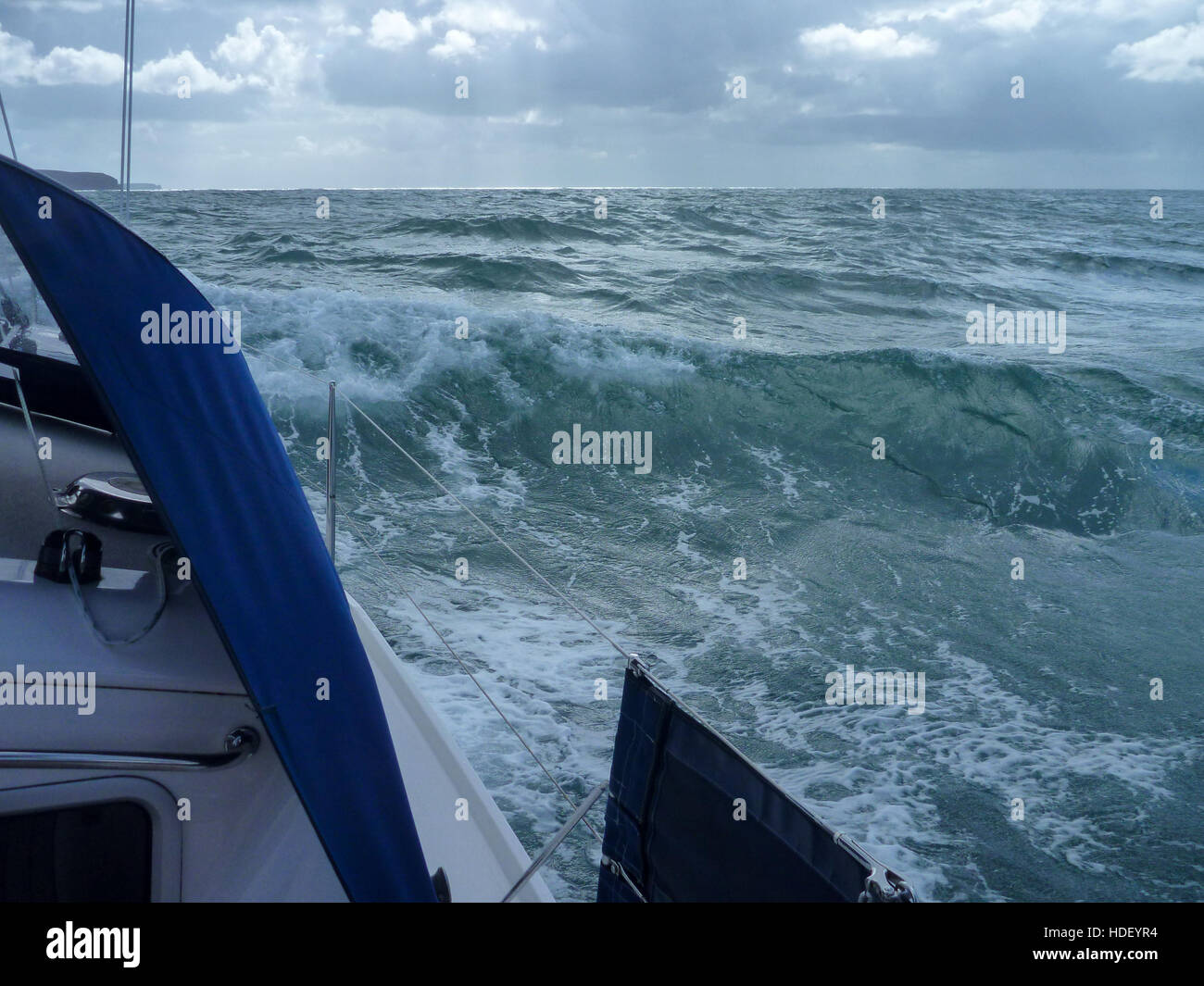 Un mare seguenti si impadronisce di uno yacht a vela su una giornata d'estate. Schiuma bianca sul mare verde sotto un cielo blu con nuvole bianche. Foto Stock