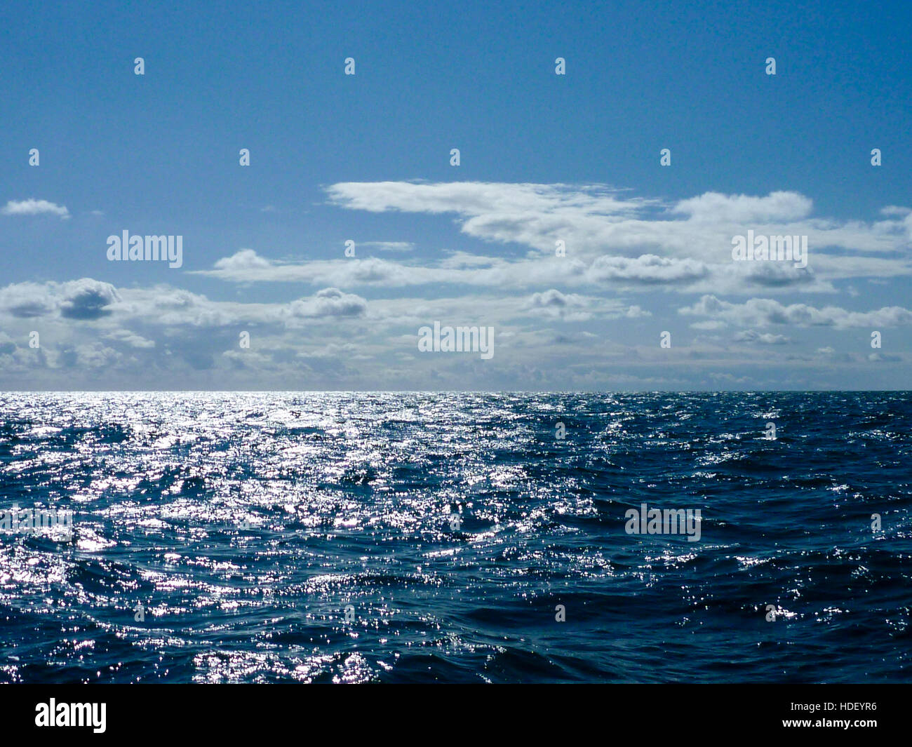 Nuvole bianche in un cielo blu riflessa in un increspato azzurro del mare Foto Stock