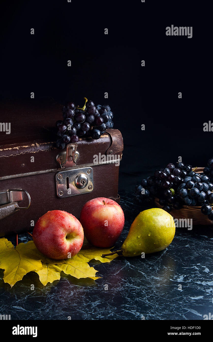 Frutte mature mele, pere e diversi giallo Foglie di autunno sul marmo scuro dello sfondo. L'uva matura nel cestello giallo e il vecchio caso sul retro dello sfondo. Foto Stock