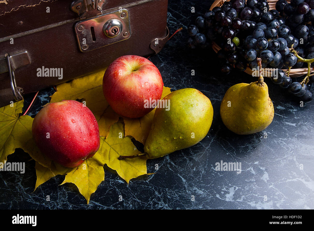 Frutte mature mele, pere e diversi giallo Foglie di autunno sul marmo scuro dello sfondo. L'uva matura nel cestello giallo e il vecchio caso sul retro dello sfondo. Foto Stock