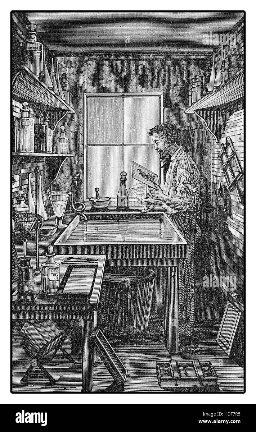 Fotografo a lavorare in una camera oscura, elaborazione sensibile alla luce di materiali fotografici per la stampa Foto Stock