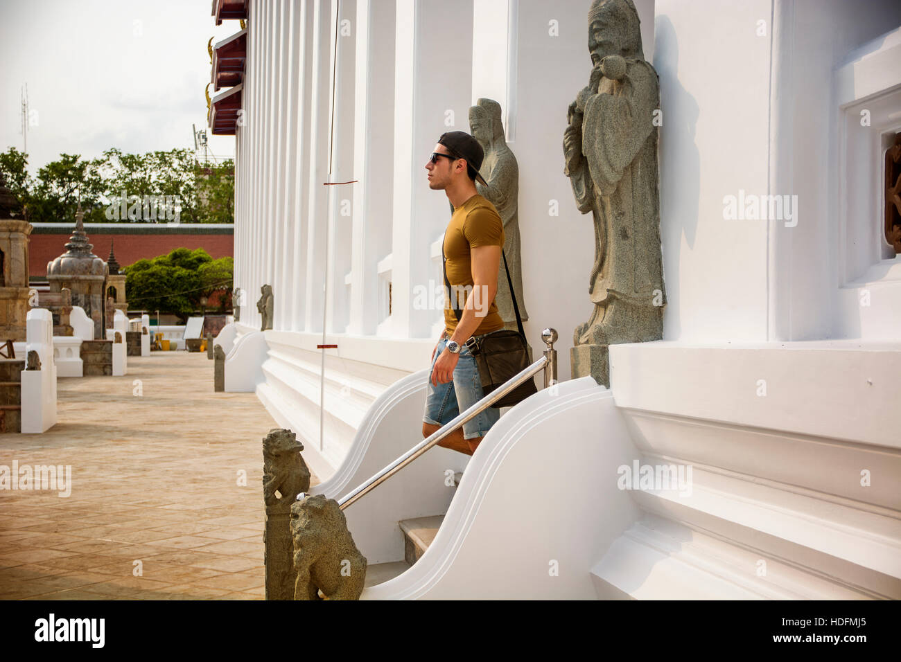 Vista laterale del giovane uomo che cammina giù per le scale del tempio buddista a Bangkok, in Thailandia e guardando dritto. Foto Stock