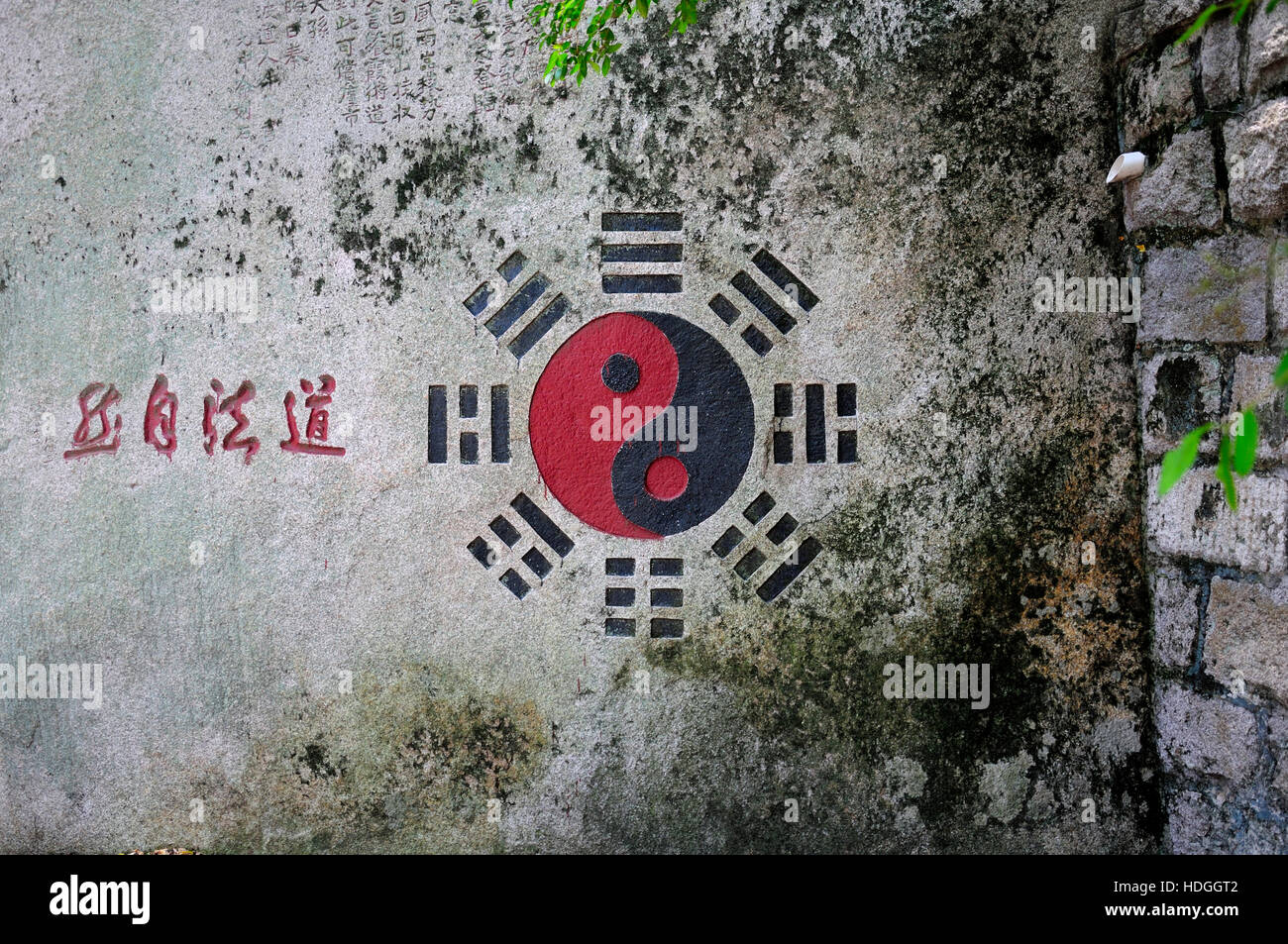 I caratteri cinesi dao fa zi ran significato dalla luce della natura nei pressi di un nero e rosso yin yang simbolo in importanti in Taosim su un muro di pietra Foto Stock