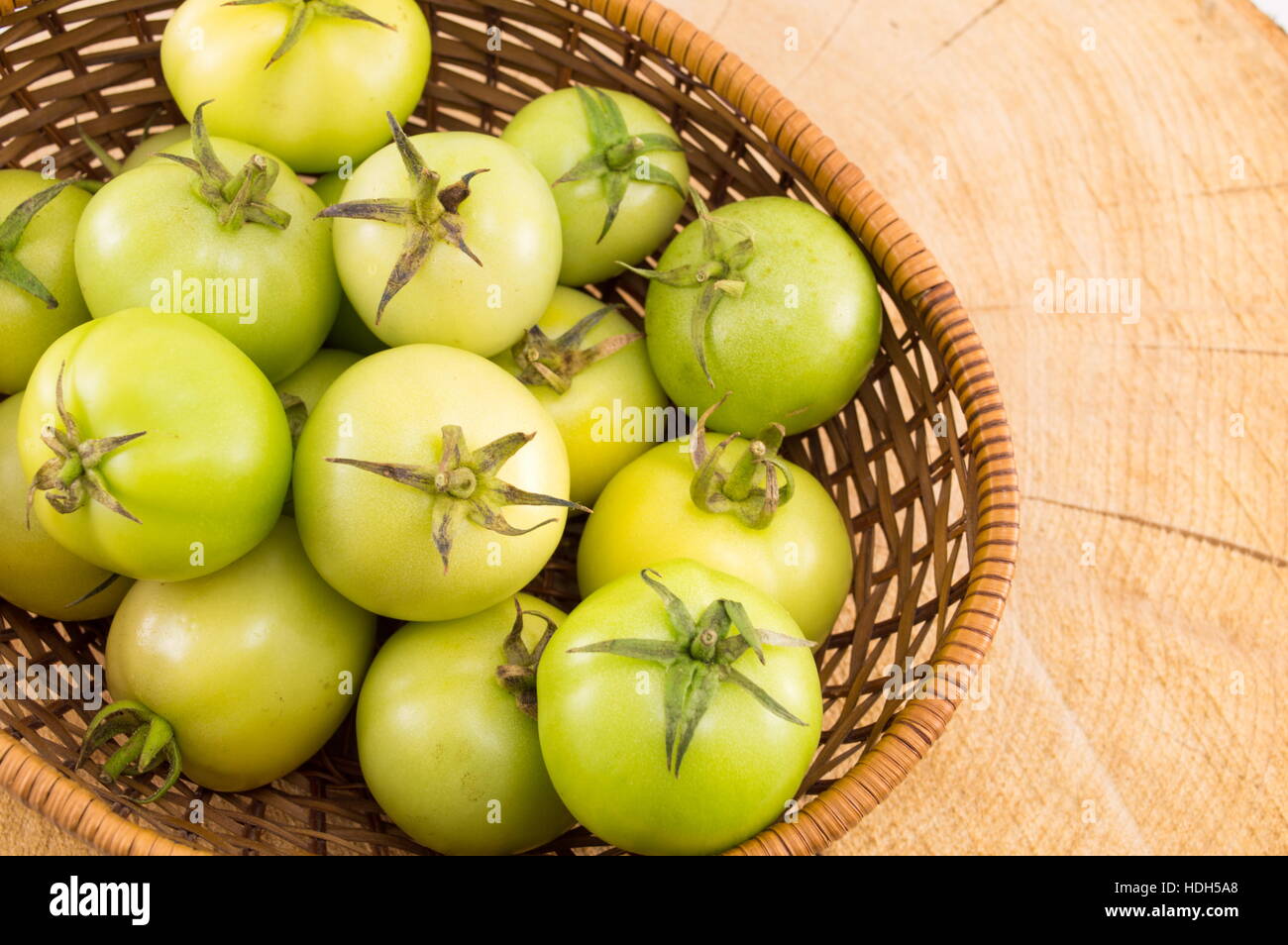 Pomodori verdi in un cesto di vimini su un tavolo di legno Foto Stock