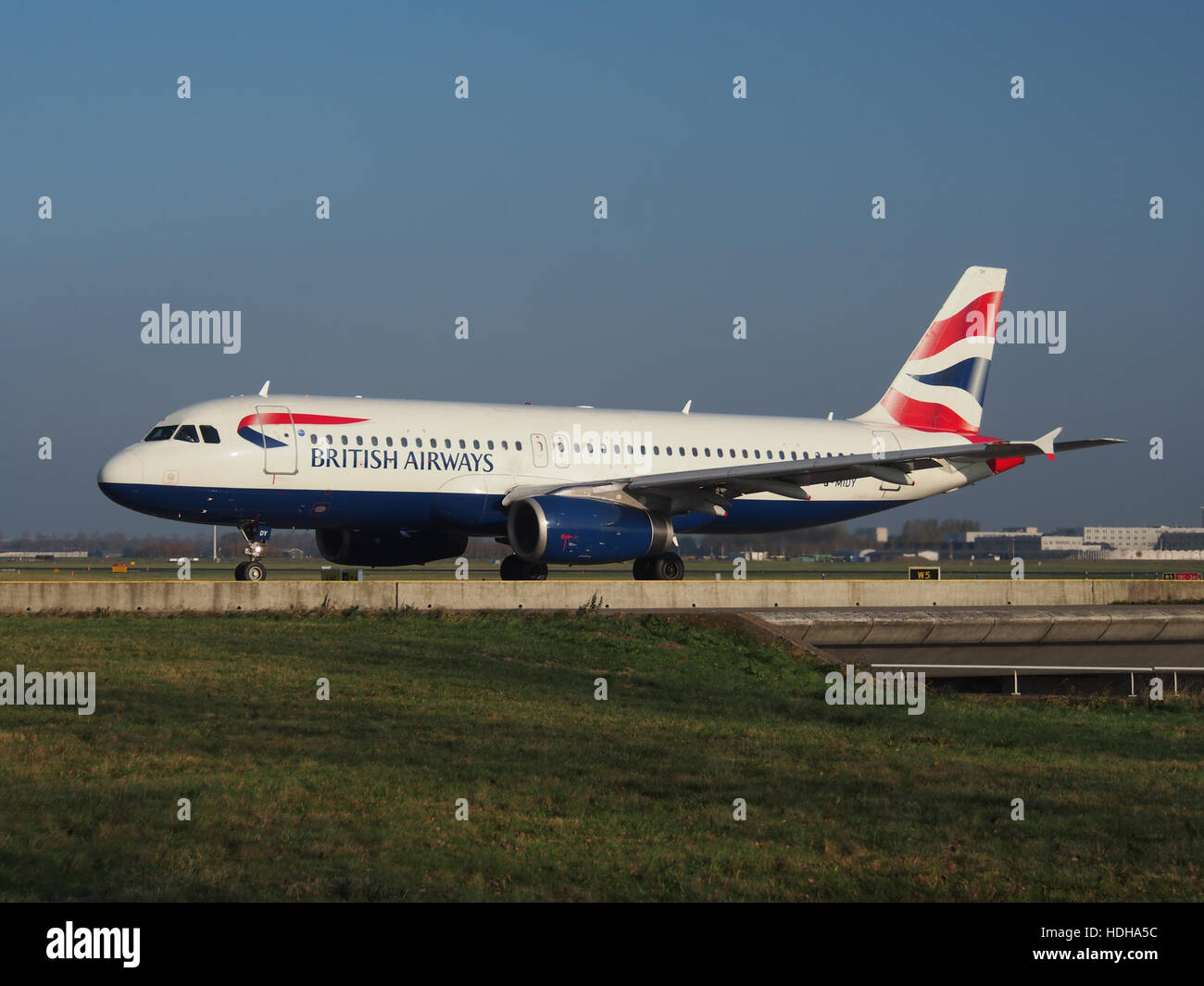 Il British Airways Airbus A320-232, registrato G-MIDY, viene catturato in rullaggio sulla pista dell'aeroporto di Schiphol, in preparazione della partenza. Questo aereo, con il numero di costruzione 1014, fa parte della famiglia A320 nota per la sua efficienza nei voli a corto e medio raggio. Foto Stock