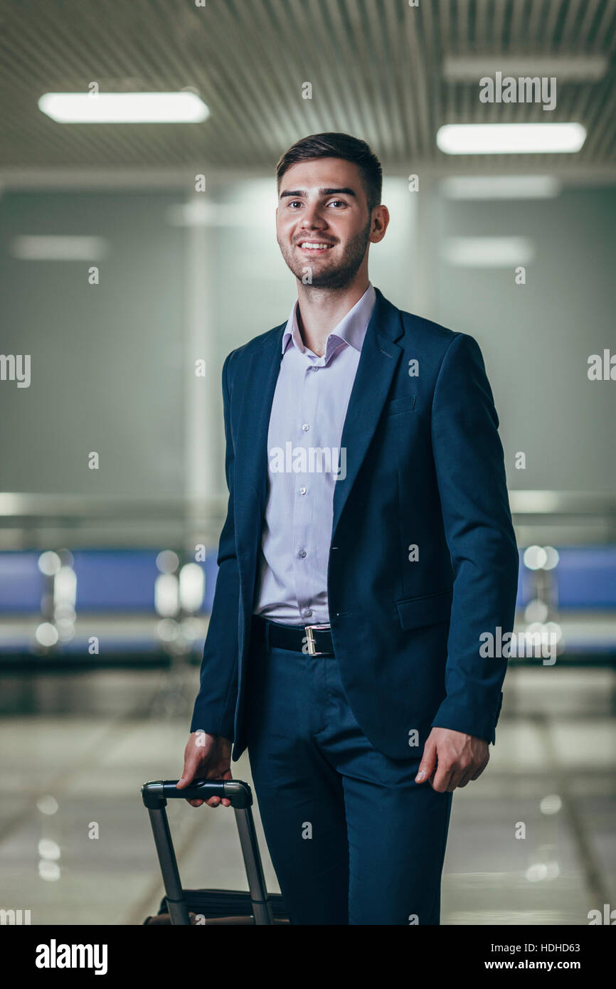 Sorridente giovane imprenditore con bagagli che guarda lontano dall aeroporto Foto Stock