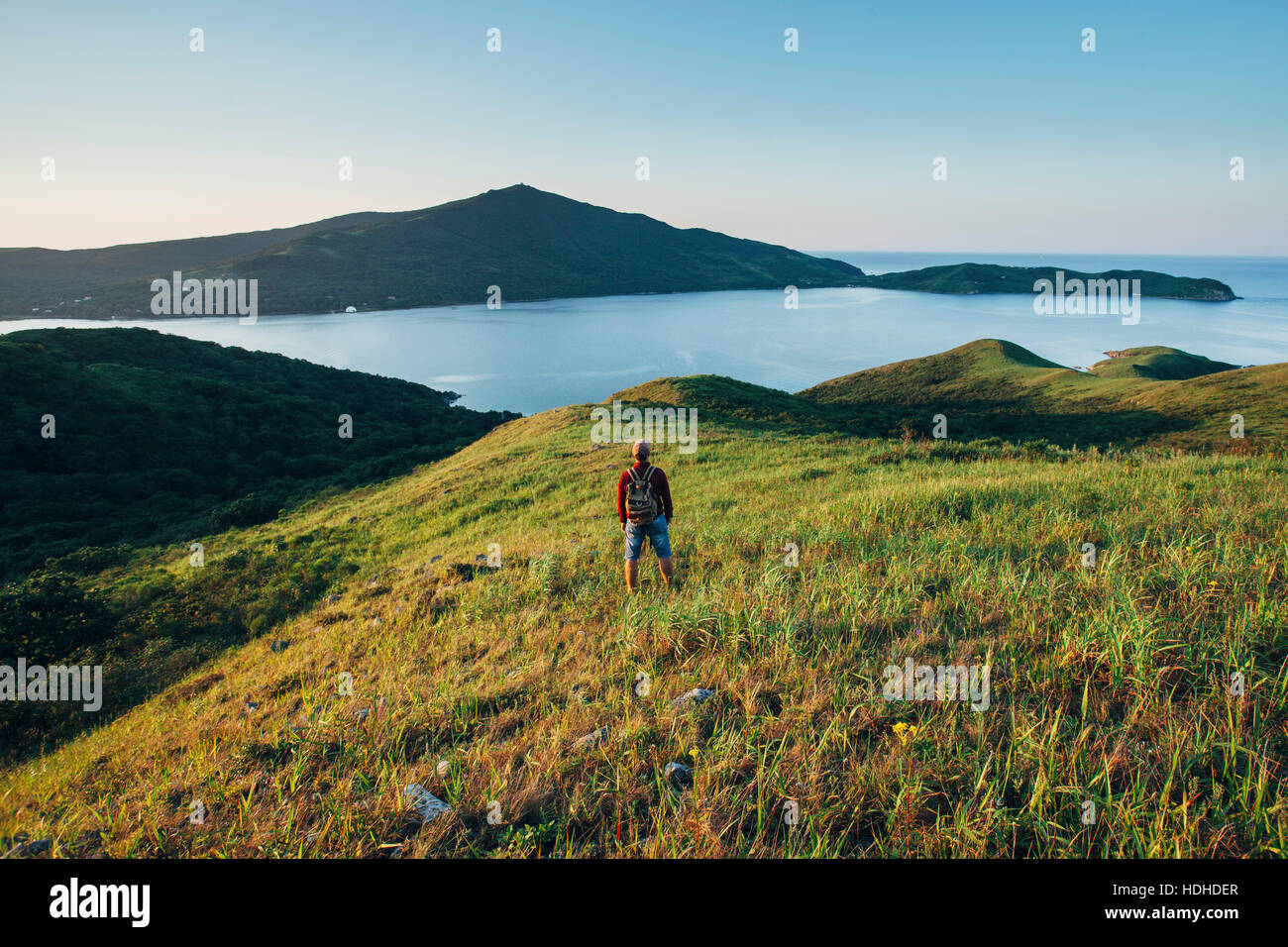 Vista posteriore di un escursionista in piedi sul campo erboso mentre guardando il mare orientale contro sky Foto Stock