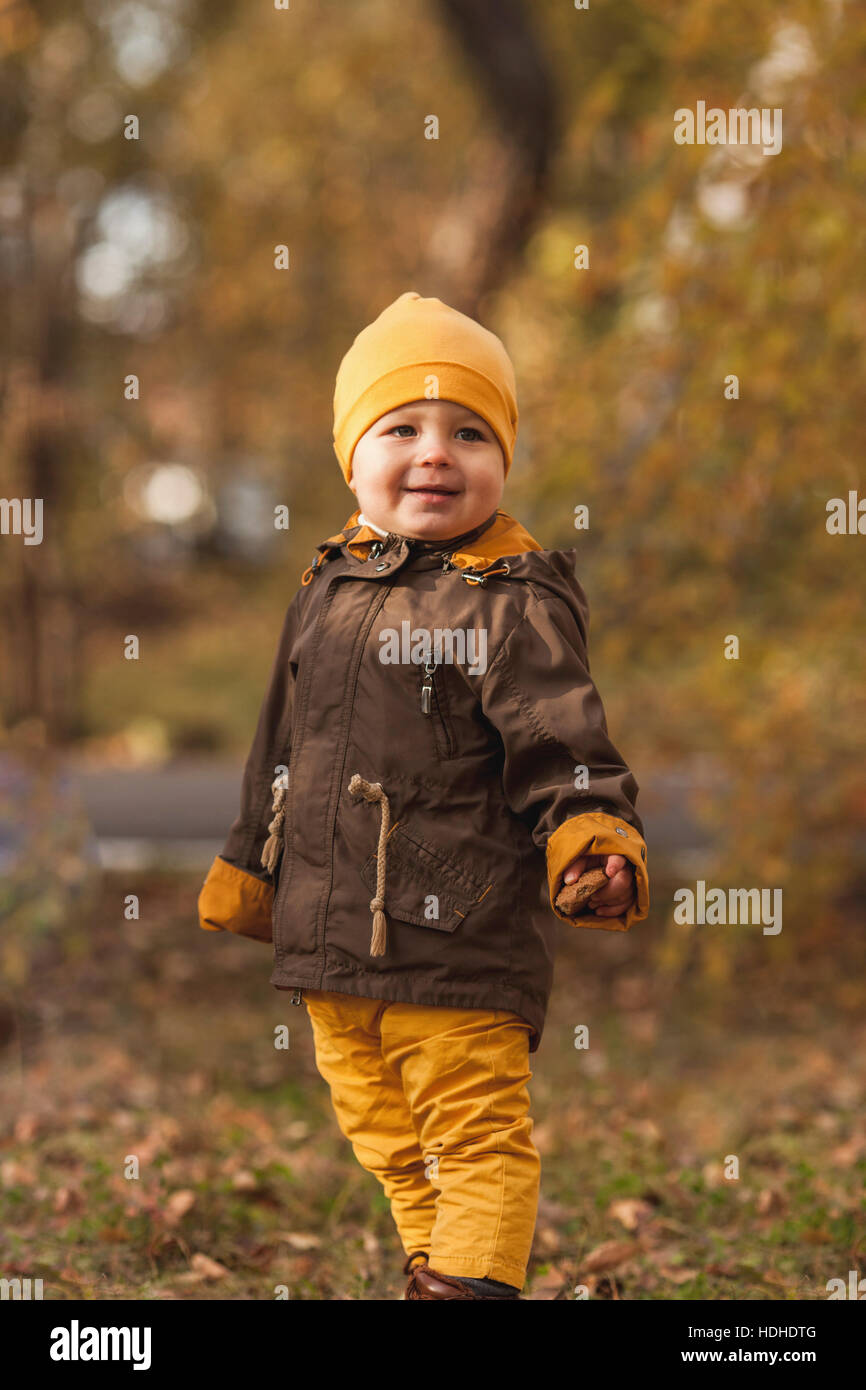 Sorridente baby boy guardando lontano rimanendo in posizione di parcheggio durante l'autunno Foto Stock