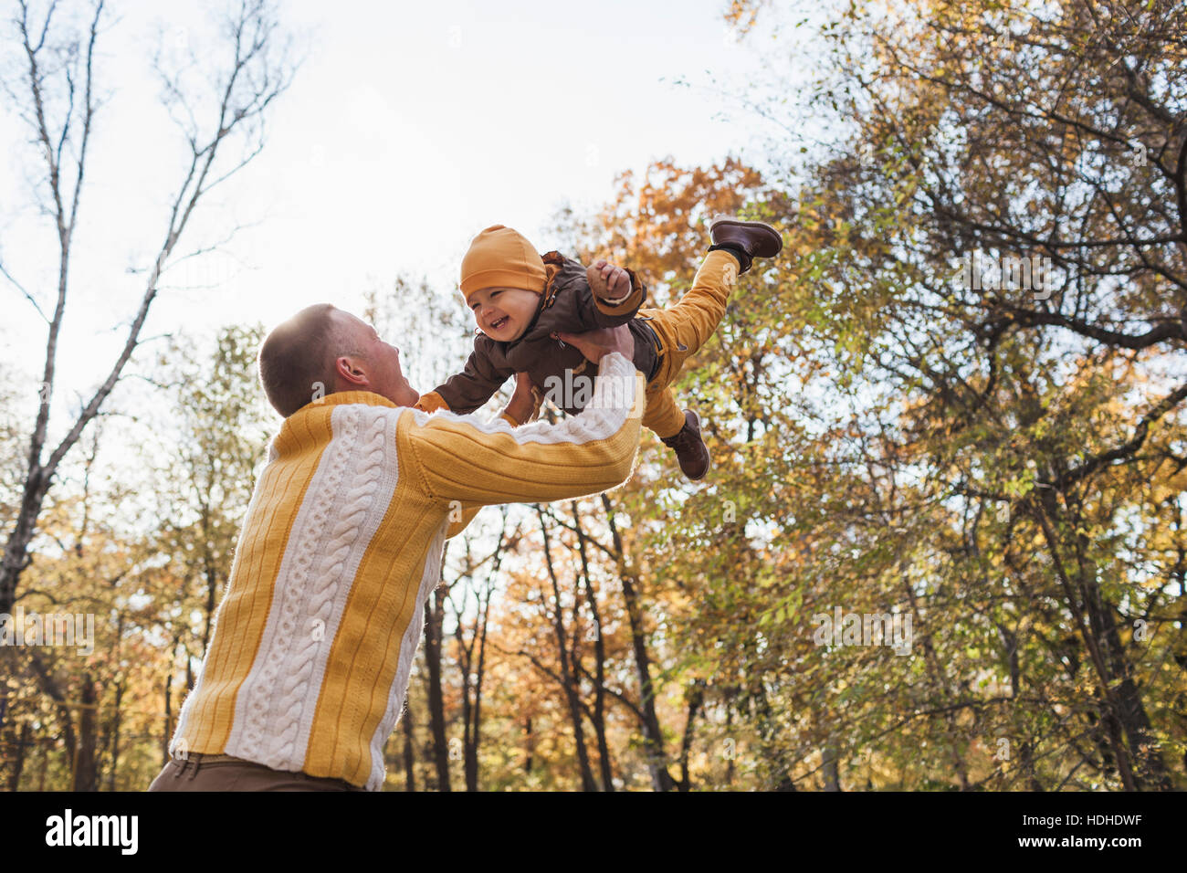 Basso angolo di vista allegra sollevamento uomo baby boy al parco durante l'autunno Foto Stock