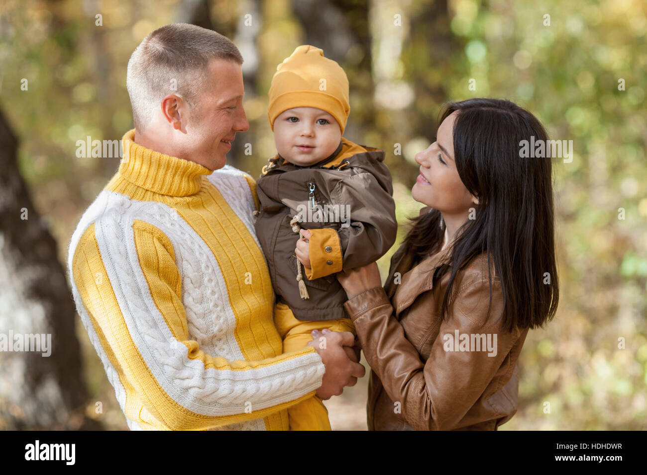 Sorridente genitori guardando baby boy permanente, mentre nel parco durante l'autunno Foto Stock